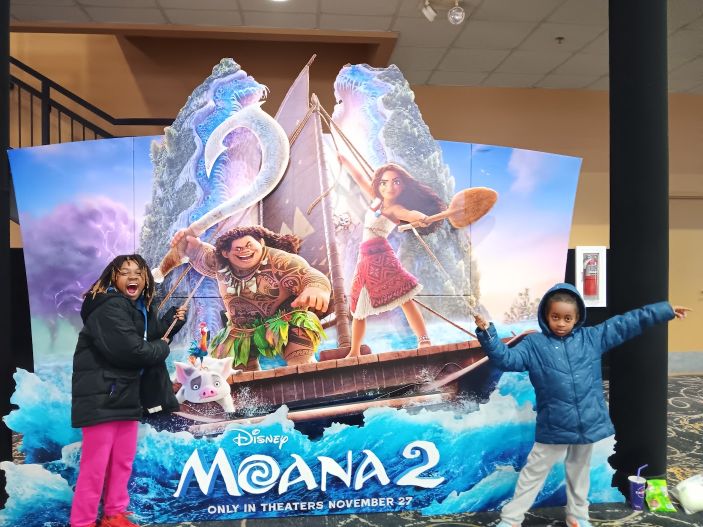Sorilbran's daughters posing with the ropes on the interactive Moana 2 boat display in a theater lobby